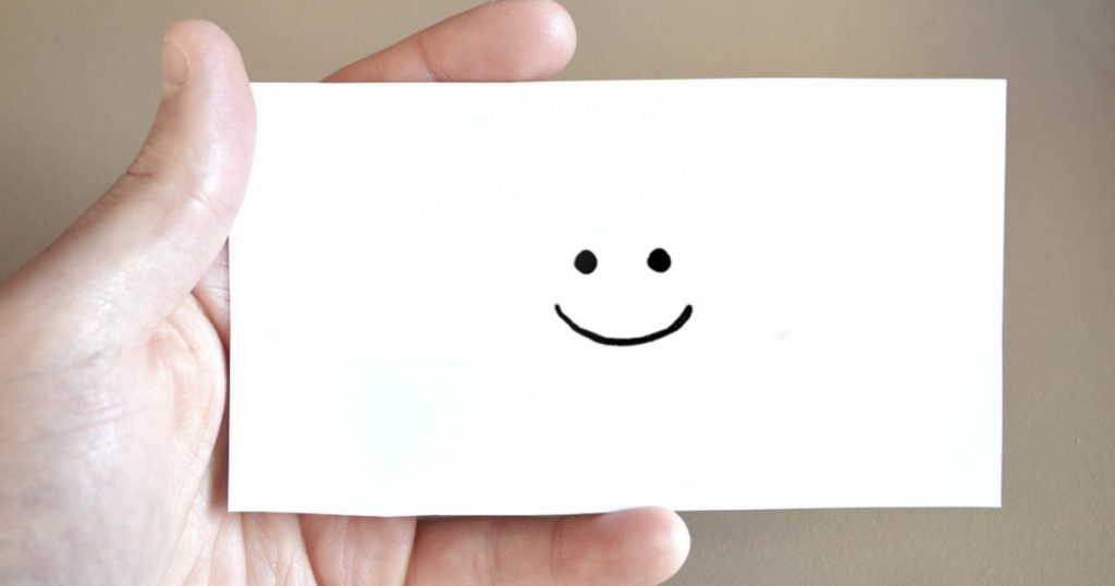A hand holding a paper card with a drawn smiley face